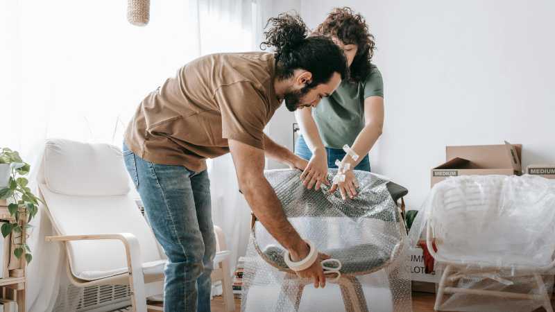 A couple carefully packs a chair with bubble wrap in their apartment, preparing for moving day., tags: antiques - pexel